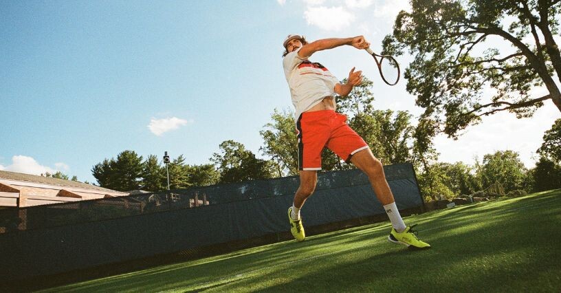 Osoba hrá tenis na tráve v športovej obuvi