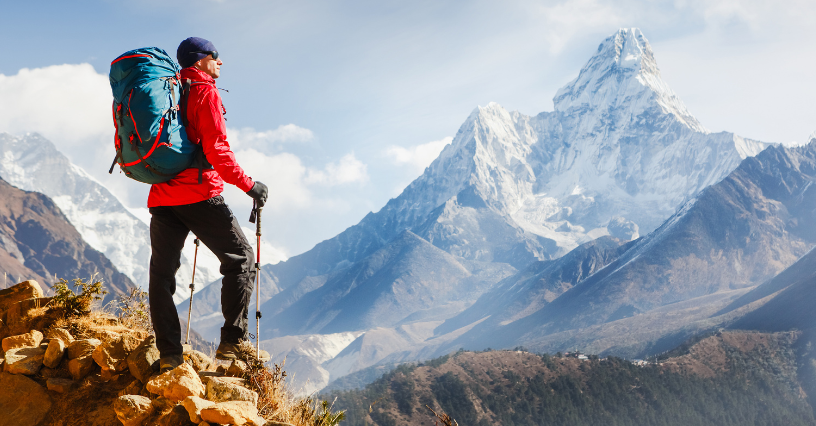 Osoba s batohom stojí na skale s pohľadom na horskú scenériu