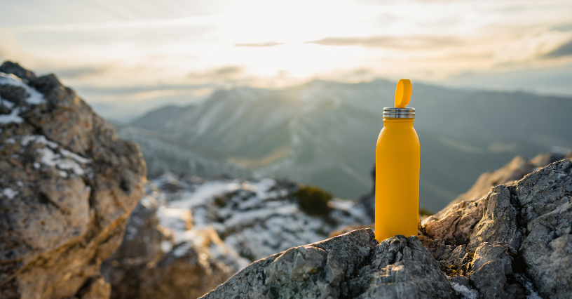 Na obrázku je žltá fľaša na skalách s panorámou hôr v pozadí