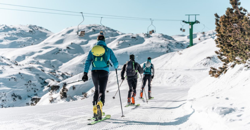 Traja lyžiari idú do svahu s lyžami na nohách