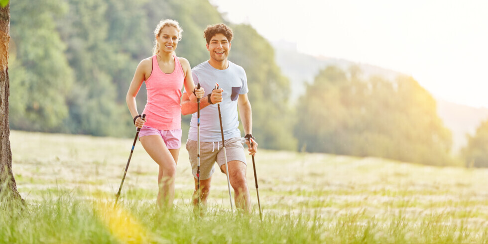Dvaja ľudia kráčajú s trekkingovými palicami na lúke