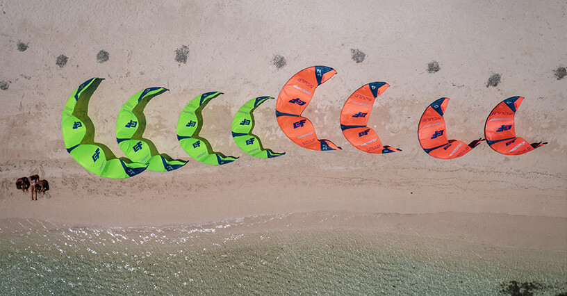 Rôzne veľkosti kitesurfingových krídel zoradené na pláži pri vode