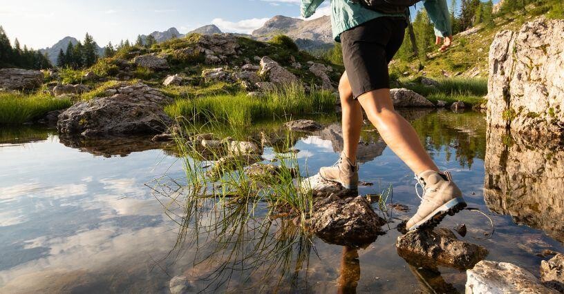 Osoba prechádza cez kamene v horskom potoku s turistickou obuvou