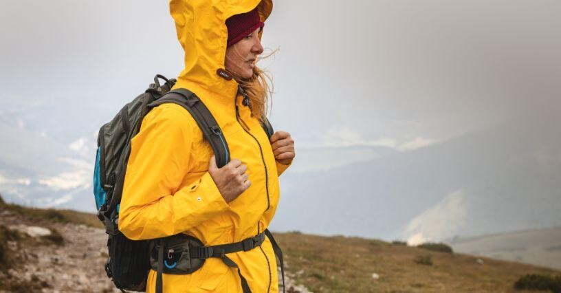 Osoba stojí na horskej trase v žltej bunde s batohom