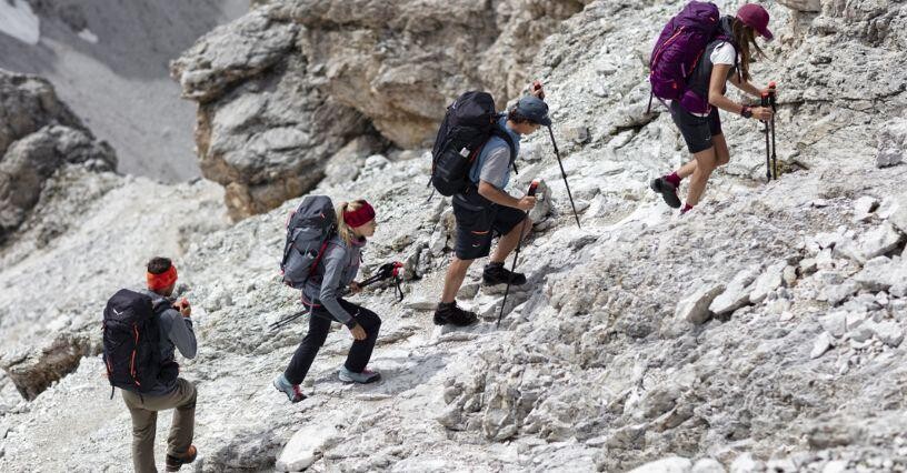 Skupina turistov s batohmi šplhá po skalnatom svahu na túre