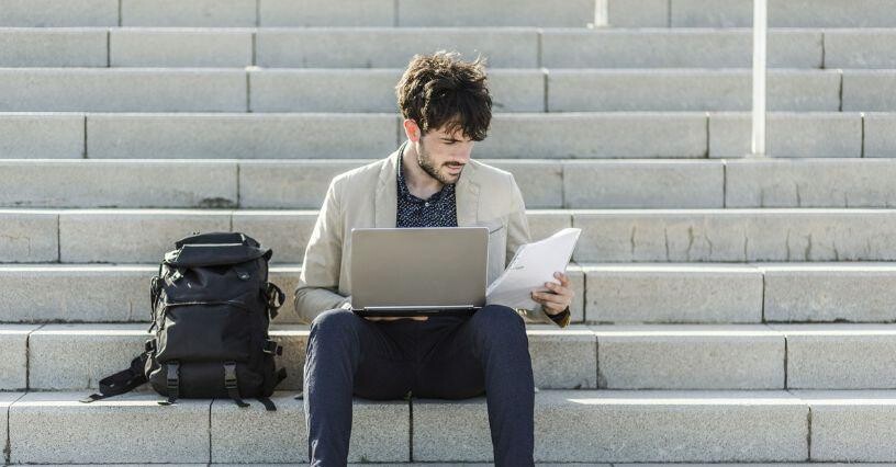 Osoba s notebookom a batohom sedí na schodoch