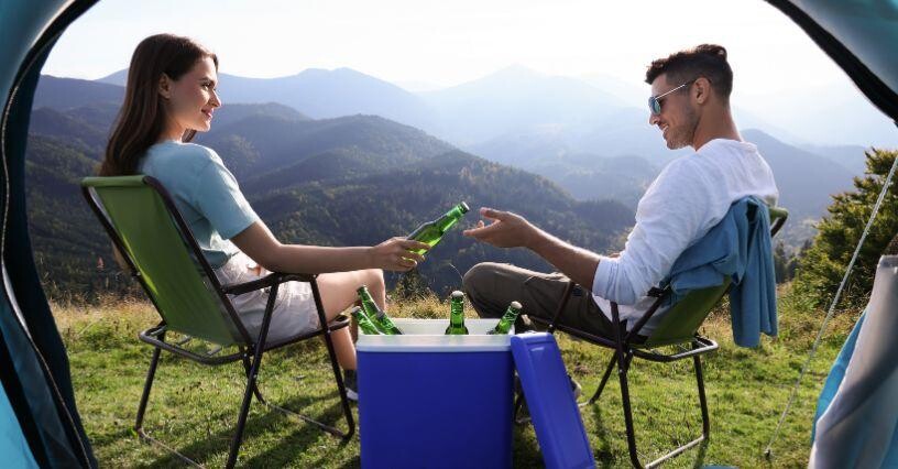 Dvaja ľudia relaxujú v prírode s nápojmi na kempingových kreslách